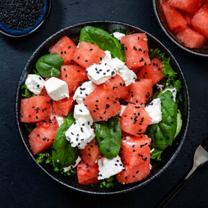 Un bowl que contiene cubos de sandía, espinacas y queso