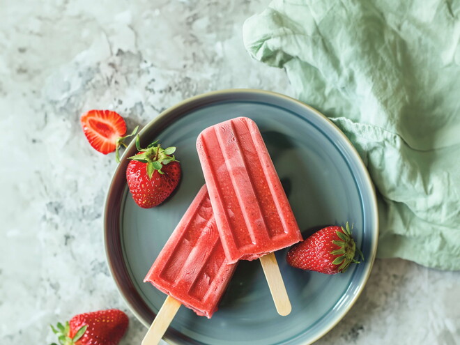 En plato, en primer plano estan colocados 2 paletas de fresas con frutas decorativas alrededor