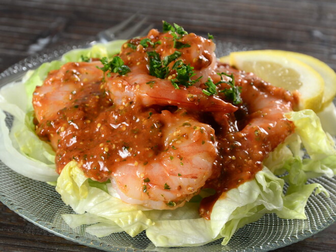 en un plato hay una base de ensalada y encima camarones con salsa