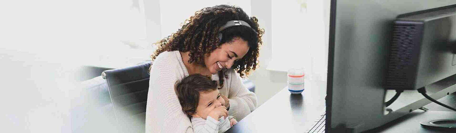 Madre sentada en su escritorio frente a su computadora con su bebé en su regazo sonriendo