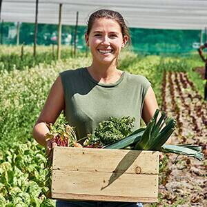 Mujer en cultivo sosteniendo caja llena de hortalizas